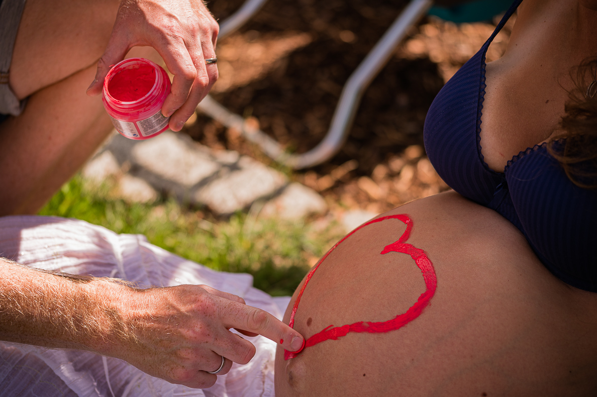 Eine schwangere Frau wird liebevoll mit einem Herz bemalt, das ihre innige Verbindung zum Baby zeigt Eine schwangere Frau wird liebevoll mit einem Herz bemalt, das ihre innige Verbindung zum Baby zeigt